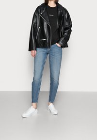 Musta nahkainen moottoripyörätakki hopeisilla vetoketjuilla, yhdistettynä mustaan t-paitaan, vaaleansinisiin farkkuihin ja valkoisiin tennareihin harmaalla taustalla.