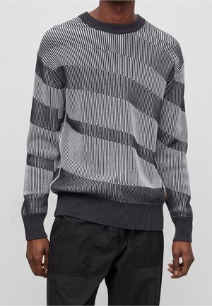 Pull en tricot avec de larges rayures horizontales noires et blanches, col rond côtelé et ourlet, avec une finition en tissu texturé.