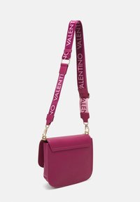 Magenta läder crossbody-väska med klaffstängning och bred justerbar rem tryckt med "VALENTINO" i vitt.