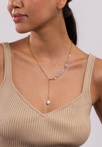 Goldene Halskette mit lila und weißen Perlen, ausgestattet mit einem Tropfenanhänger, der eine Perle enthält. Glatte Textur, geschichtetes Design und unterschiedlich große Perlen.