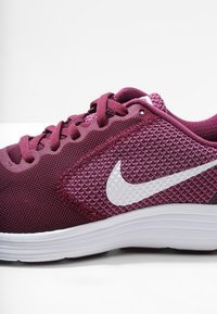 Baskets de sport bordeaux avec tige en mesh, accents texturés, logo Swoosh blanc et semelle blanche rembourrée. Design à lacets avec couture renforcée.