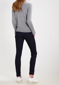 Suéter gris de punto con mangas largas, jeans ajustados de color azul oscuro y zapatillas blancas. Textura suave y diseño ajustado.