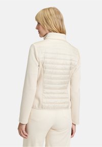 Jasna kremowa kurtka z pikowanym tyłem, stójką oraz miękkim materiałem. Projekt obejmuje gładkie rękawy oraz dopasowaną sylwetkę.