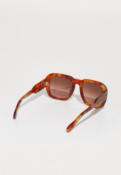 Lunettes de soleil écaille de tortue avec une monture carrée, des verres dégradés marron et des accents en or sur les branches.