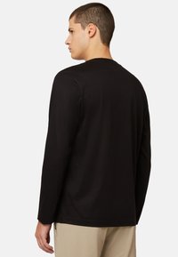 Must mustaga pikkade varrukatega T-särk, millel on ümar kaelus, valmistatud pehmest kangast, sirge lõikega ja minimaalse õmblustega, kantud beežide pükstega.