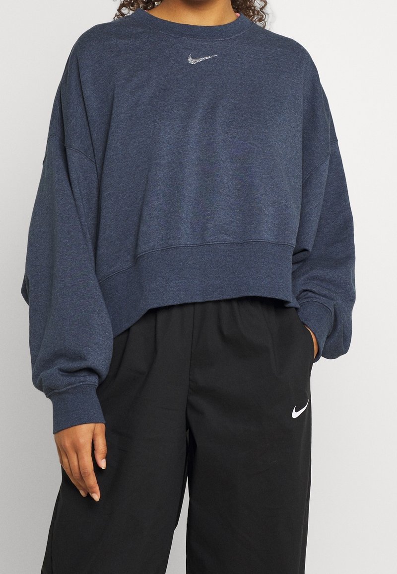 Tmavě modrá krátká mikina s dlouhými volnými rukávy a kulatým výstřihem. Na hrudi je malé bílé logo Nike.