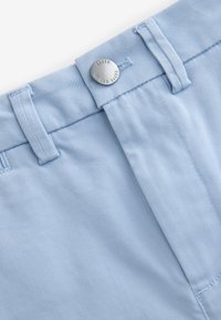 Hellblaue Stoffhose mit glatter Textur, Knopfverschluss und Gürtelschlaufen. Nähte sind entlang der Kanten sichtbar.