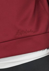 Burgundia sweatshird sujuva tekstuuriga, millel on vastavates niitides tikitud "Attitude" tekst, kihituna valgete ja mustade riiete peal.