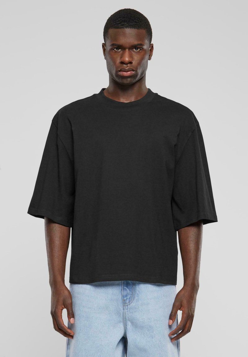 Black oversized t-shirt with short sleeves, crew neckline, and a smooth cotton texture. Paired with light blue denim shorts.