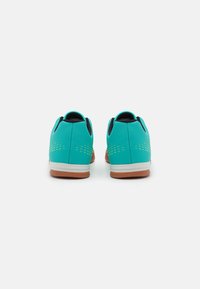 Zapatillas deportivas en color turquesa con una textura suave, acentos en negro y una suela de goma. Diseño perforado notable en la parte superior.