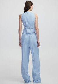 Top senza maniche di un blu chiaro, con un design aderente e un piccolo fiocco sul retro, abbinato a pantaloni larghi coordinati.