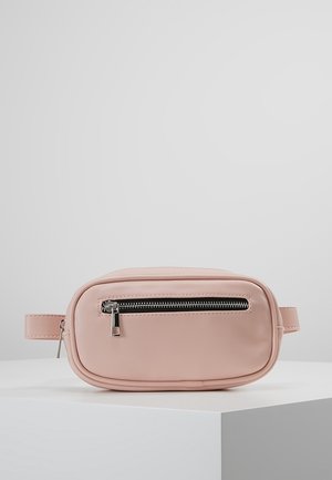 Sac banane rectangulaire rose clair avec poche avant à fermeture éclair, fermeture éclair argentée et sangle latérale, présenté sur un plateau blanc.