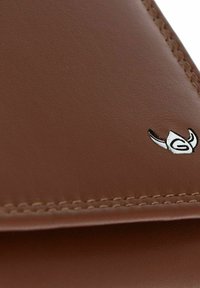 Coin de portefeuille en cuir marron avec couture détaillée et petit emblème argenté présentant des cornes stylisées et la lettre "G".