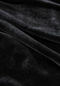 Black velvet fabric featuring a soft, smooth texture with subtle sheen. The material displays folds and a rich, deep color.