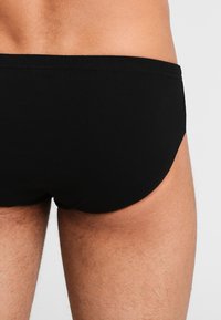 Shorts de bain noirs en tissu doux, dotés d'une texture lisse et d'un design simple et minimaliste avec une taille élastique.