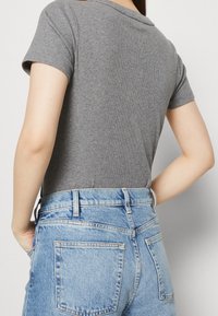 Grå ribbad kortärmad skjorta som är kombinerad med högmidjade ljusblå denimjeans med bakfickor och en urtvättning.