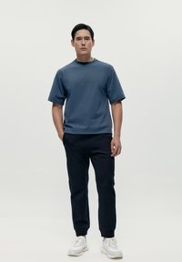 Mörkblå bomullströja med korta ärmar, i kombination med marinblå smala sweatpants och vita sneakers, med en minimalistisk design.