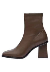 Bottine en cuir brun avec un bout pointu, un dessus ajusté et un talon carré épais. Présente une texture lisse et un minimum de détails de couture.