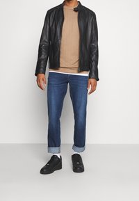 Giacca di pelle nera, camicia testurizzata marrone chiaro, jeans blu con risvolto, e sneakers nere. Linee pulite ed elementi di design semplici.