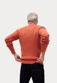 Suéter de punto naranja con un patrón texturizado, cuello redondo y puños acanalados, usado sobre unos jeans oscuros, visto desde la parte de atrás.