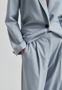 Svetlo modro oblečeno srajco, ki vključuje strukturiran blazer z enim gumbom in široke hlače s plitvami in stranskimi žepi.