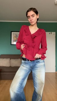 Bluză roșie, cu volane, cu mâneci lungi și talie strânsă, combinată cu blugi albaștri largi, cu aspect estompat și croială lejeră.