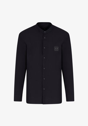 Maglietta nera a maniche lunghe con colletto alla mandarina, chiusura frontale con bottoni e una patch quadrata con logo sul lato sinistro del petto. Tessuto liscio.