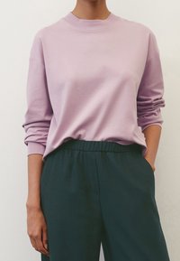 Lavender sweatshirt with a round neckline and long sleeves, paired with dark green elastic-waist trousers. Soft fabric and relaxed fit.