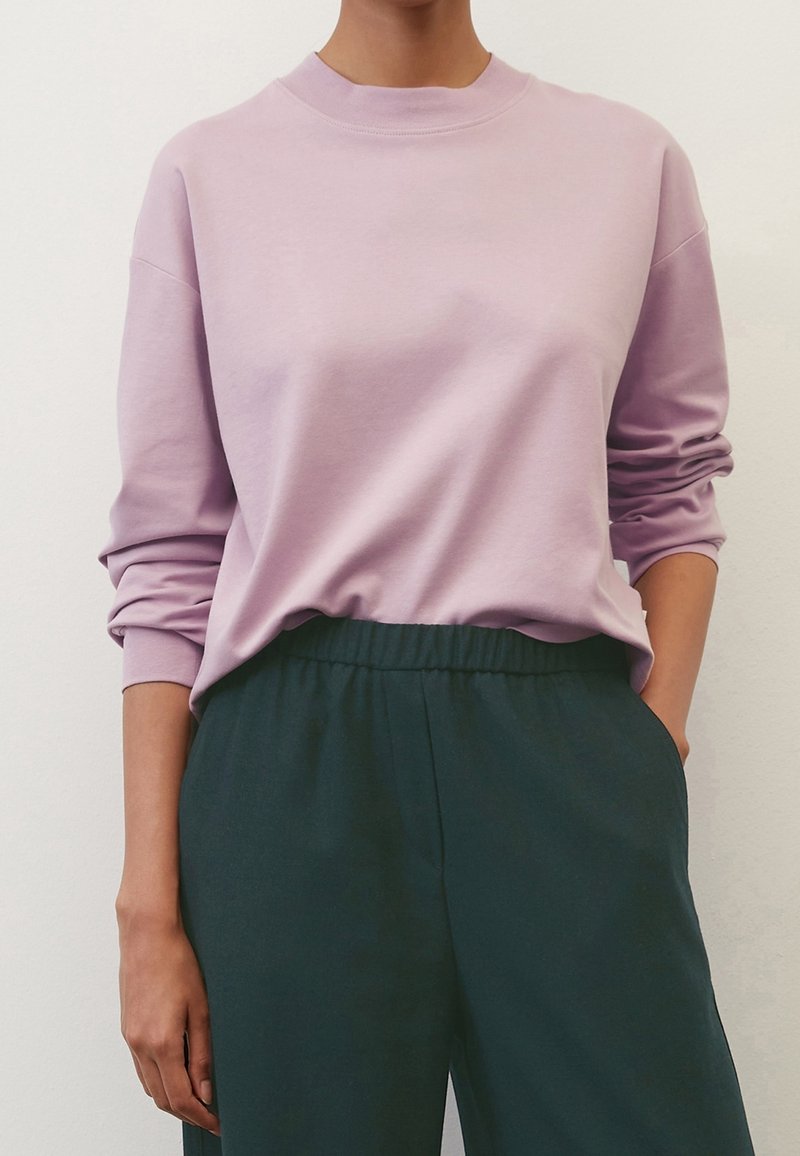 Lavender sweatshirt with a round neckline and long sleeves, paired with dark green elastic-waist trousers. Soft fabric and relaxed fit.
