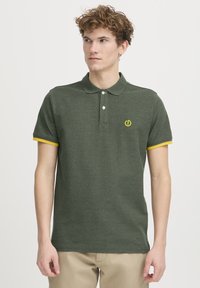 Mørkegrøn polo-shirt lavet af struktureret stof. Har en gulstribet krave, en tre-knaps lukning og et logo på brystet.