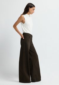 Pantalons larges marron avec une surface texturée, ornés de petits détails en clous. Associés à un top blanc sans manches ajusté.