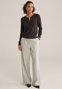 Temno rjav teksturiran kardigan z gumbi spredaj, kombiniran s svetlo sivimi širokimi hlačami z visokim pasom in špicastimi rjavimi čevlji z visokim peto.