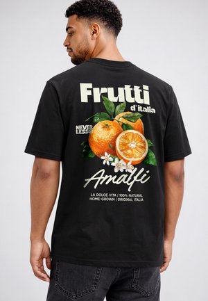 Man wearing black t-shirt with graphic of oranges, white flowers, and text "Frutti d'Italia Amalfi" on the back against a plain background.