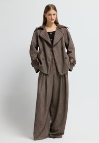 Giacca doppiopetto in misto lana marrone con dettagli in pelle marrone, colletto ampio e pantaloni larghi coordinati, caratterizzati da una finitura testurizzata.