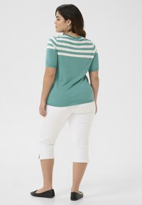 Pulover teal cu dungi orizontale albe, mâneci scurte, asortat cu pantaloni capri albi și balerini negri. Textură netedă și design casual.