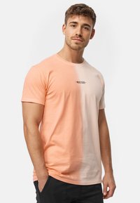 Camiseta de manga corta en degradado de melocotón y rosa claro. Presenta un cuello redondo y un pequeño logotipo en negro en el pecho. Material de algodón.