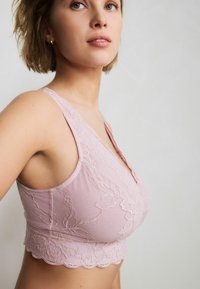 Bralette in pizzo rosa soft con tessuto testurizzato, orlo scallopato e dettagli in pizzo floreale sulle spalline e nella zona del seno.
