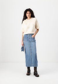 Crème trui met korte mouwen en verhoogde bloemenpatronen, gecombineerd met een hoge taille blauwe denim maxi rok met knopen aan de voorkant en zakken.