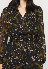 Černé šaty s květinovým vzorem v růžové, bílé a zelené barvě, s překládaným designem a dlouhými, volnými rukávy. Měkká, průhledná tkanina.