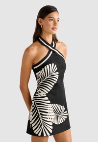 Rochie neagră cu bretele halter, având un imprimeu mare de frunză albă contrastantă, realizată dintr-un material ușor, cu o textură netedă și un design elegant.