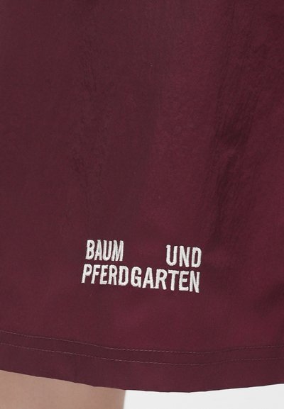 Μπορντό φούστα με υφή, που διαθέτει λευκό κεντητό κείμενο «BAUM UND PFERDGARTEN» κοντά στο τελείωμα, τονίζοντας την προβολή της μάρκας.