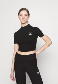 Melna ribota topiņa ar augstu kaklu, īsām piedurknēm un baltām akcentiem uz pleciem. Uz krūtīm ir balts Puma logotips.