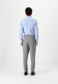 Camisa azul claro de botones, pantalones de rayas grises, tela suave, corte ajustado, piernas rectas, combinada con zapatos negros, detalle visible en la parte trasera.