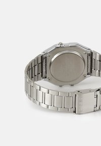 Montre Casio en acier inoxydable avec un boîtier octagonal, un bracelet en métal, une finition brossée et une boucle arborant le logo Casio. Le dos présente des détails gravés.
