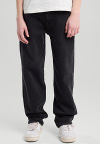 Mustat farkut, joissa on rento leikkaus, suorat lahkeet ja sileä rakenne. Yhdistetty valkoisiin tennareihin.