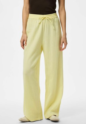 Personne portant un pantalon large ample texturé jaune clair avec une taille élastique et un cordon, associé à des chaussures beiges à enfiler.