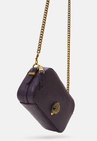 Lila texturerad handväska med en guld metallkedja, som har en dekorativ guld ögon-design på framsidan och ett blixtlås.