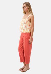 Top senza maniche con motivo floreale in giallo chiaro con accenti arancioni; abbinato a pantaloni larghi corallo; la modella indossa sandali beige.