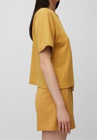 Camiseta de mezcla de algodón color mostaza con mangas cortas y cuello redondo, combinada con pantalones cortos a juego que cuentan con una cintura elástica.