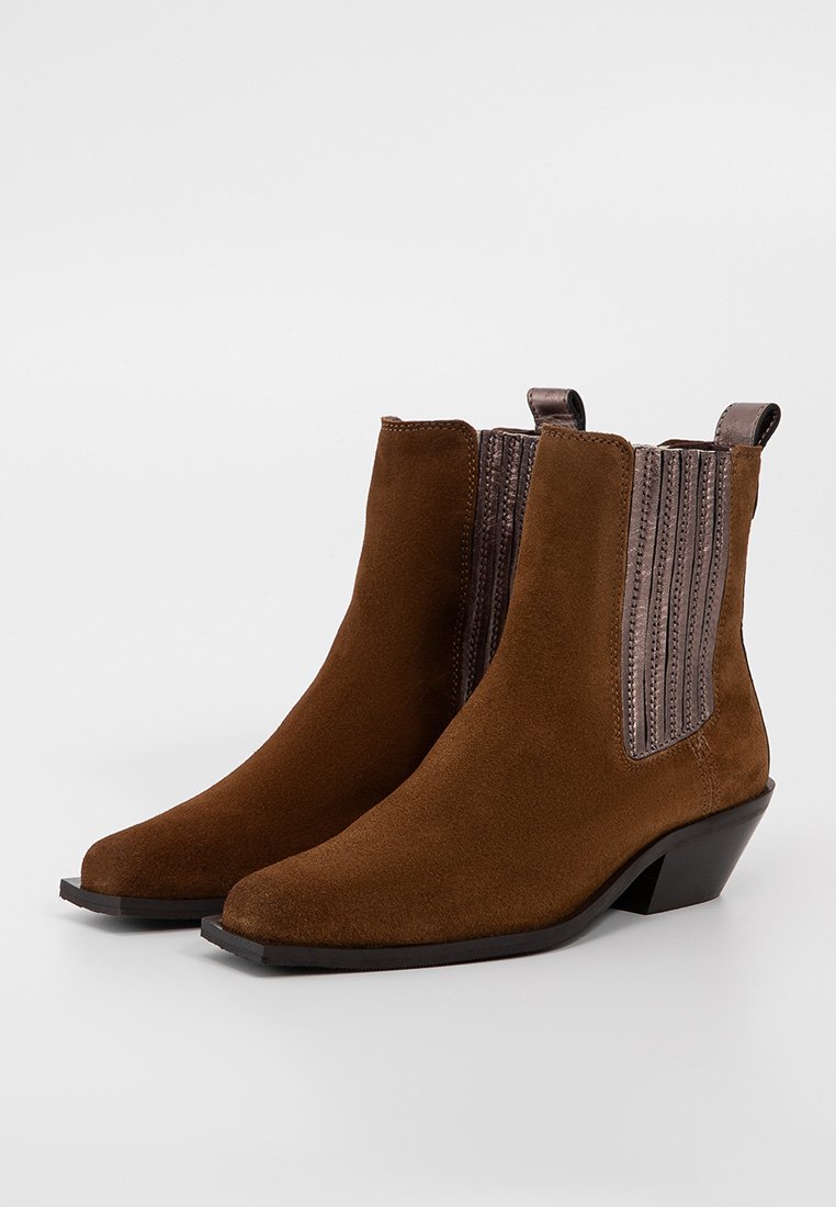 Bruine suède enkellaarsjes met ribgebreide elastische zijpanelen en een kleine hak. Puntige neus en een gladde textuur. Belangrijk detail: lus aan de achterkant.